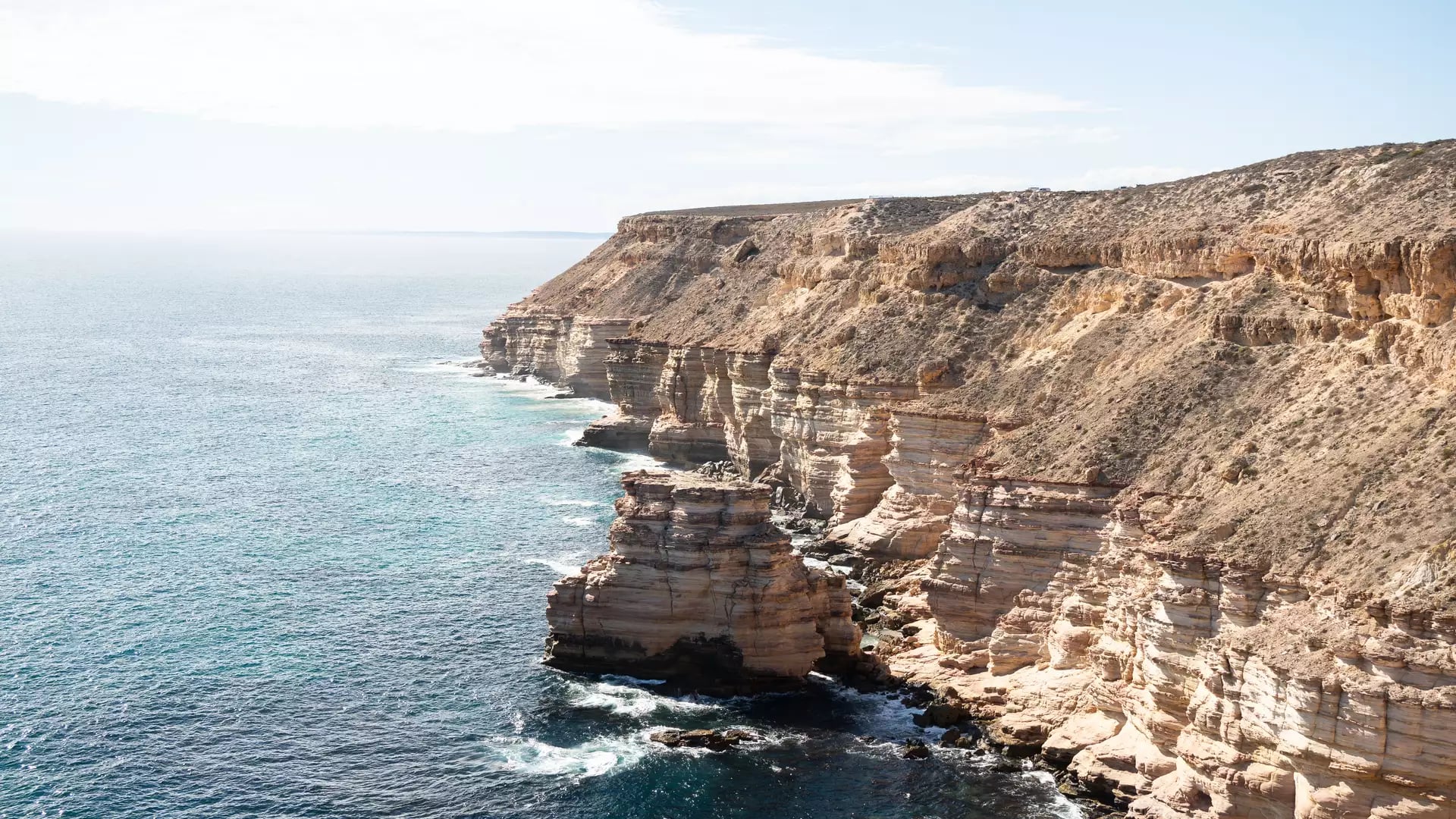 Rugged red sandstone cliffs along the Kalbarri coastline under a clear sky.