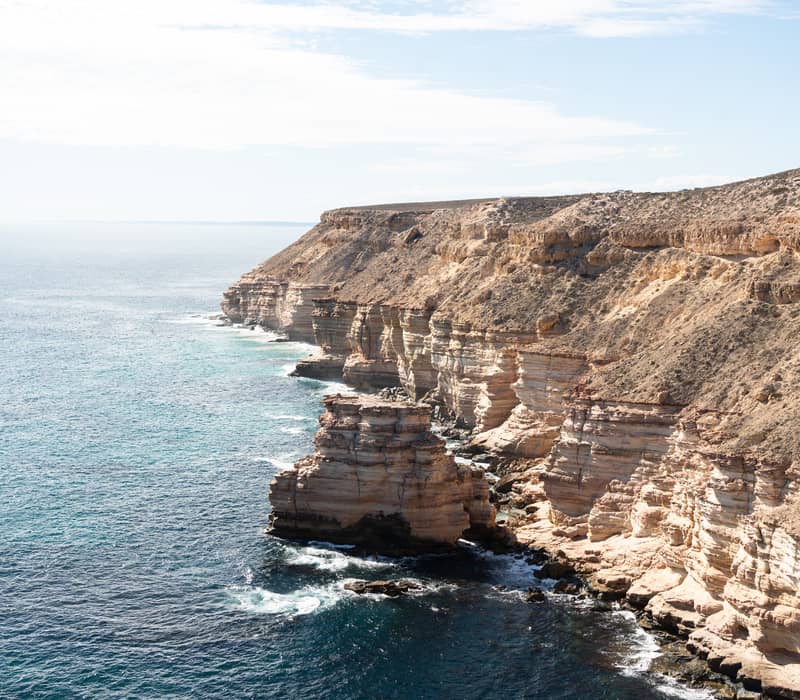 Rugged red sandstone cliffs along the Kalbarri coastline under a clear sky.
