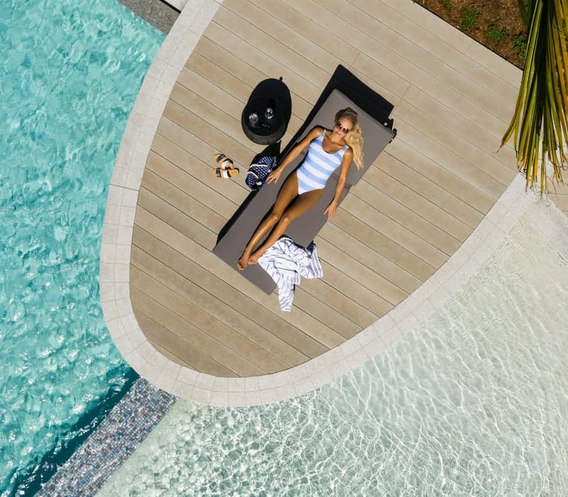 Woman sunbathing on a poolside lounger wearing sunglasses and a striped swimsuit