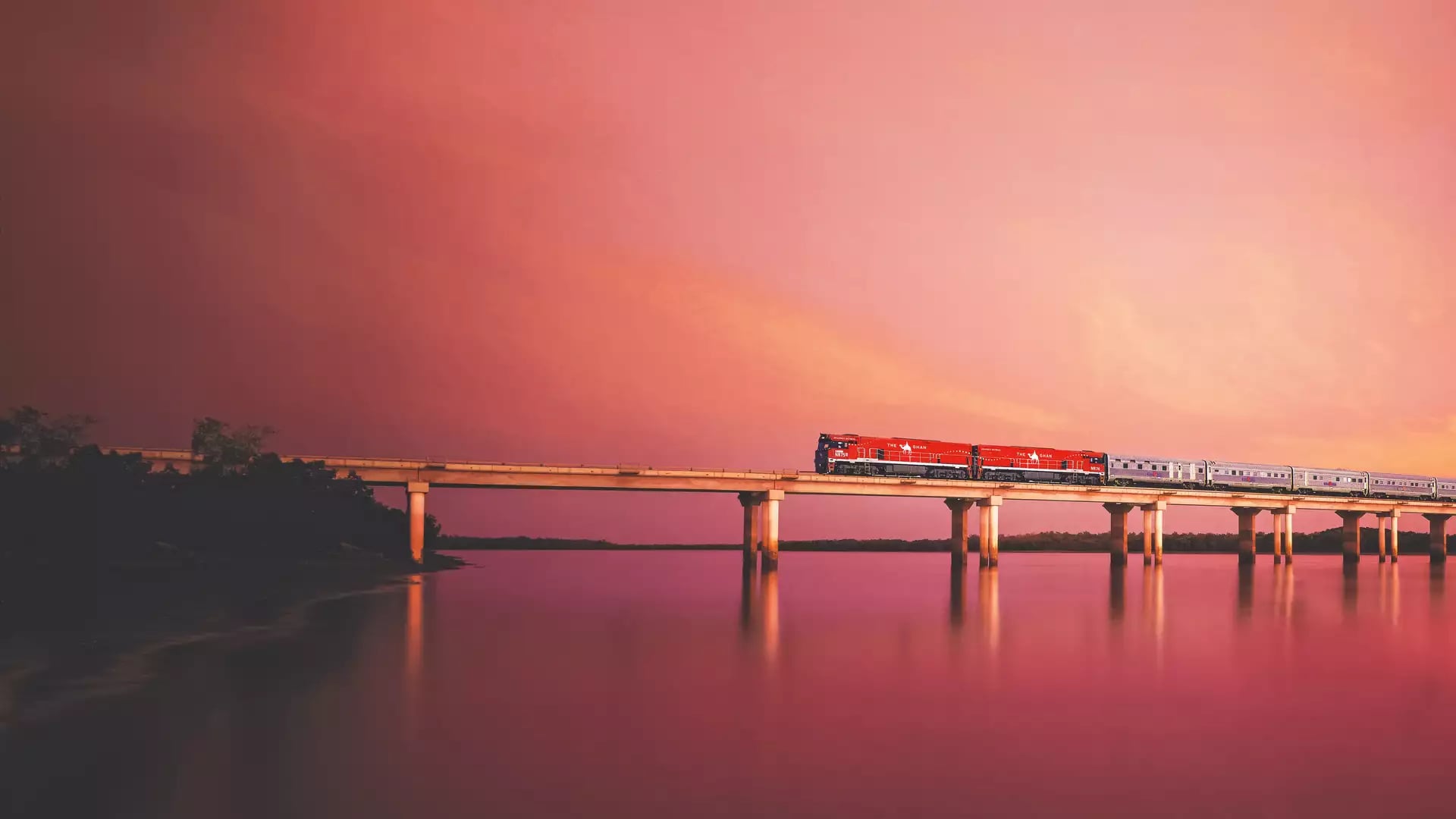 Dramatic image of The Ghan crossing a bridge over the Elizabeth River at sunset.