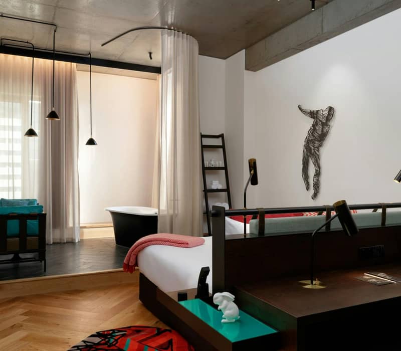 Modern hotel suite with bathtub, wooden floors, artwork on wall, and stylish furnishings.
