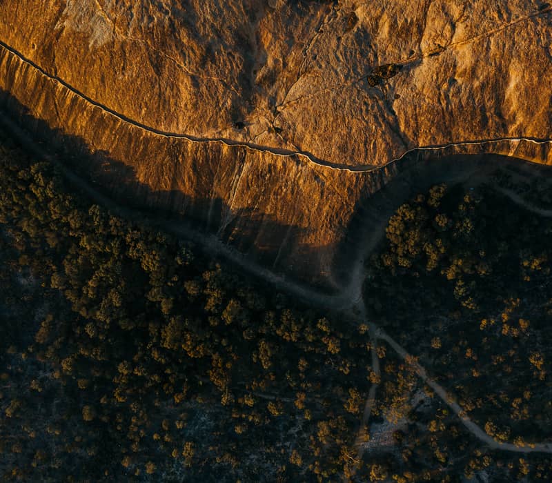 he golden light of a Wheatbelt sunset illuminates the top of the Wave Rock granite outcrop in Hyden, casting long shadows over the surrounding trees.