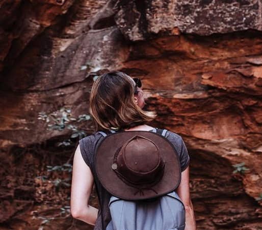 Traveler with a hat looking up at massive orange rock walls in a Kimberley gorge.