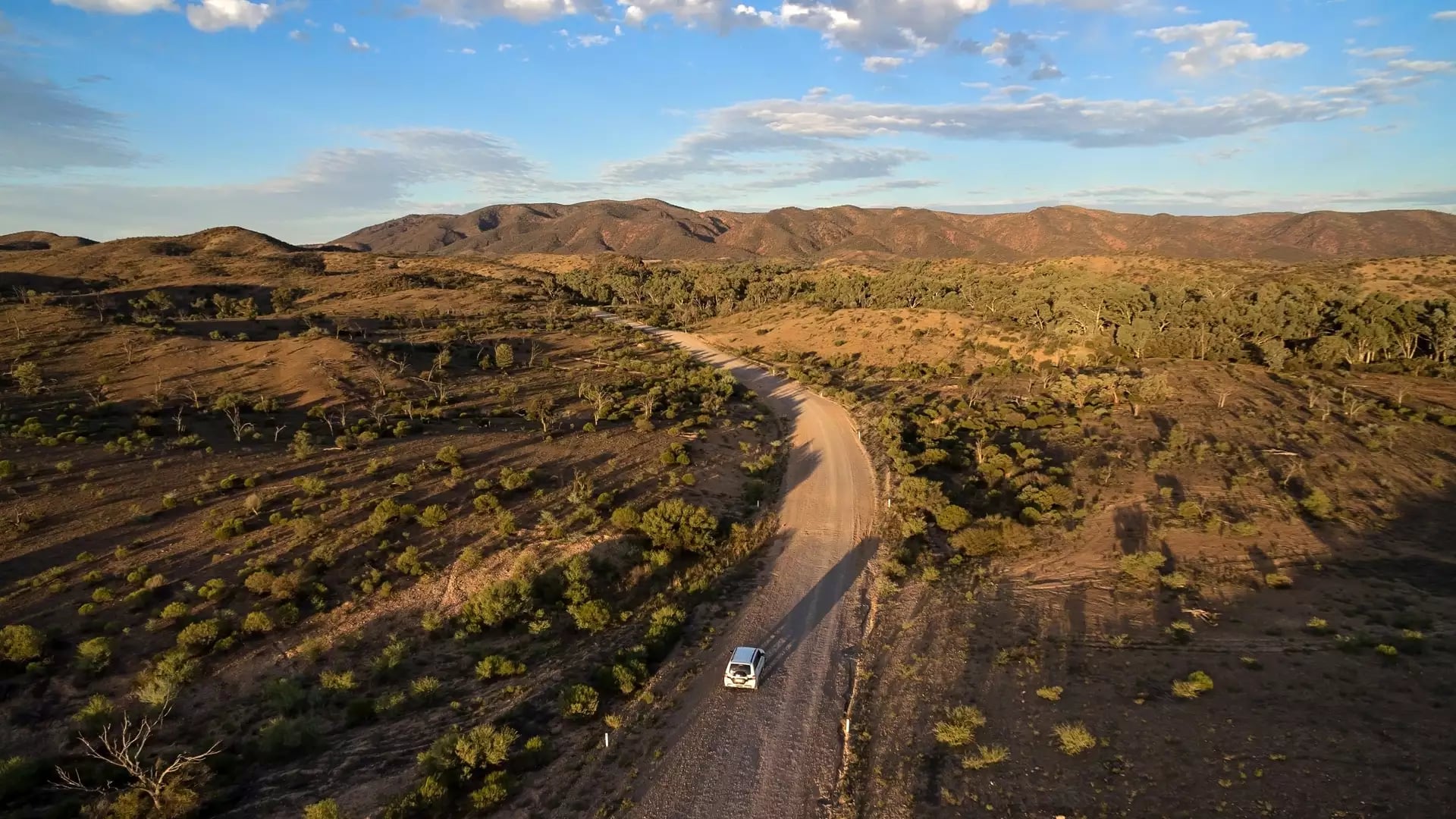 High angle view of a white car driving on a dirt road through the ancient hills of the Gammon Ranges in South Australia.