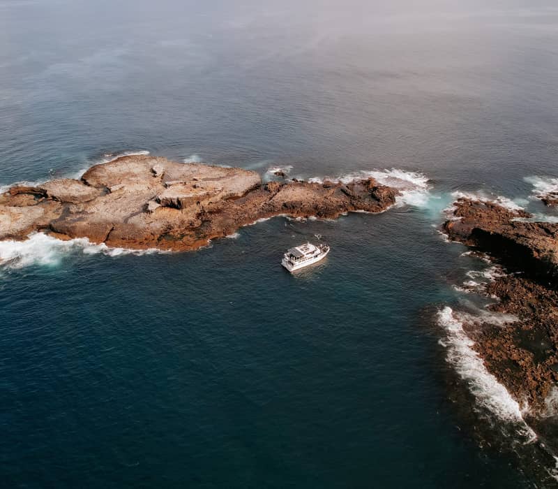 Aerial view of a white boat near rocky islands in the blue ocean at Phillip Island.