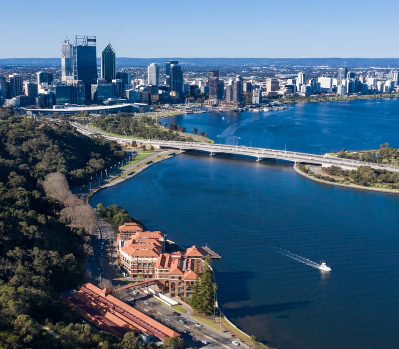 Wide aerial view of Perth city skyline and Swan River seen from the forested hills of Kings Park.