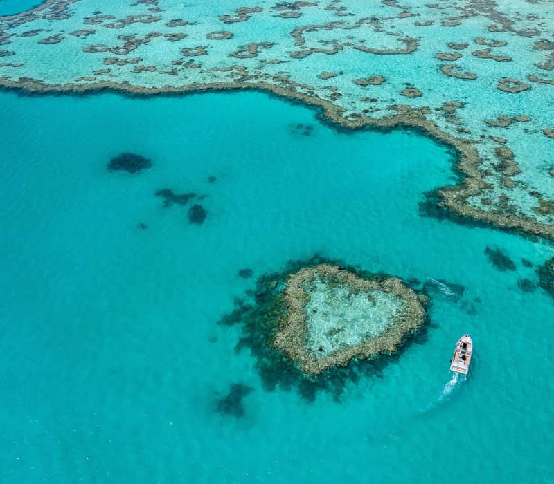 An aerial view captures the natural heart-shaped coral formation known as Heart Reef in the crystal-clear turquoise waters of the Whitsundays.