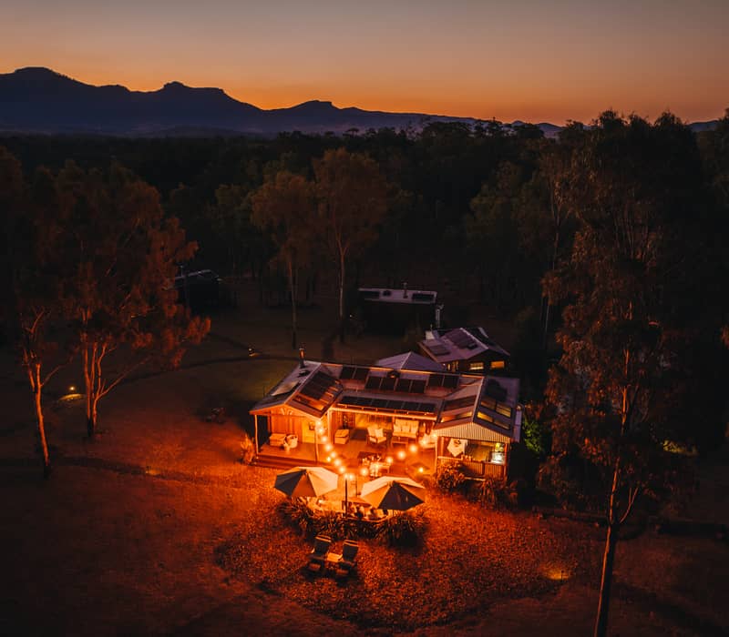 Warm glowing lights of a boutique timber cabin at dusk with a sunset mountain silhouette in the Scenic Rim.