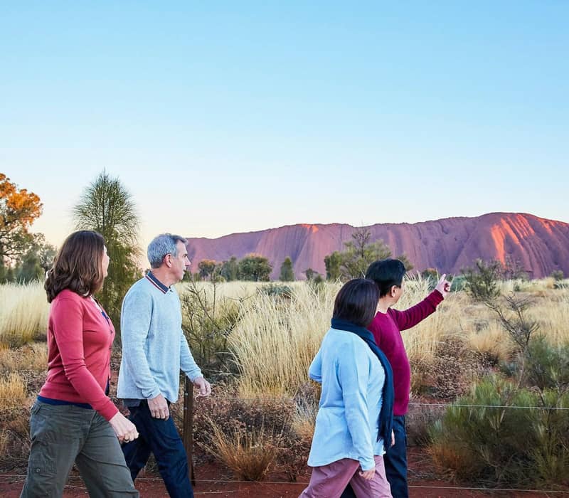 Travelers on a guided walking tour at Uluru-Kata Tjuta National Park during the golden hour.