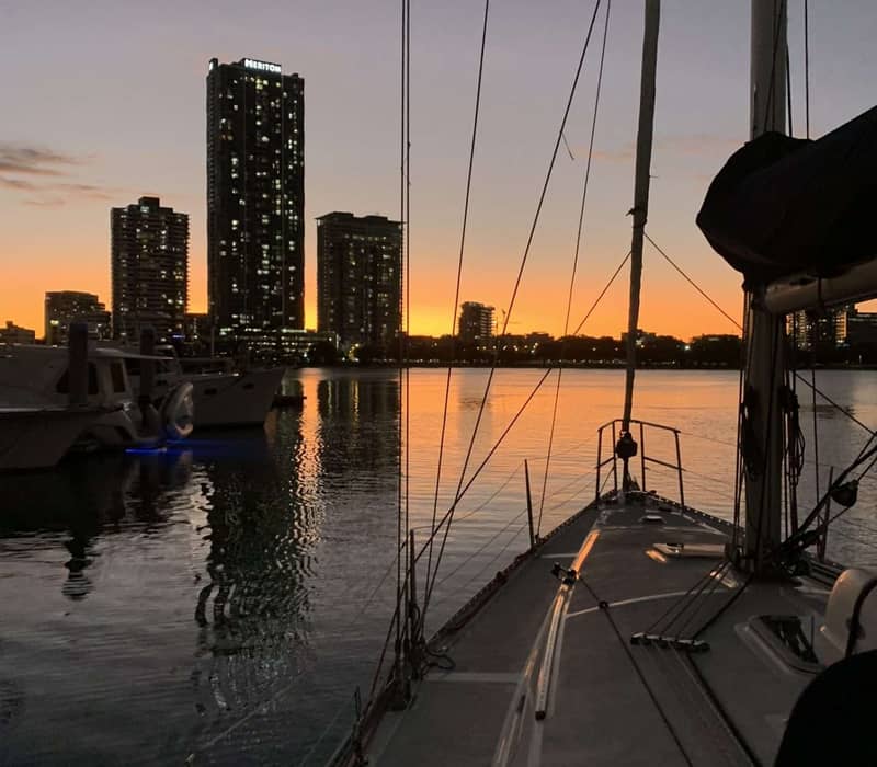 View from a sailboat of a city skyline across the water at sunset