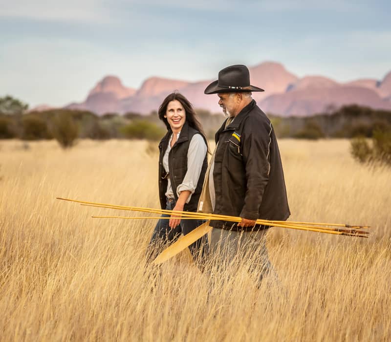 A guide and tourist walking through the Red Centre landscape with traditional spears.