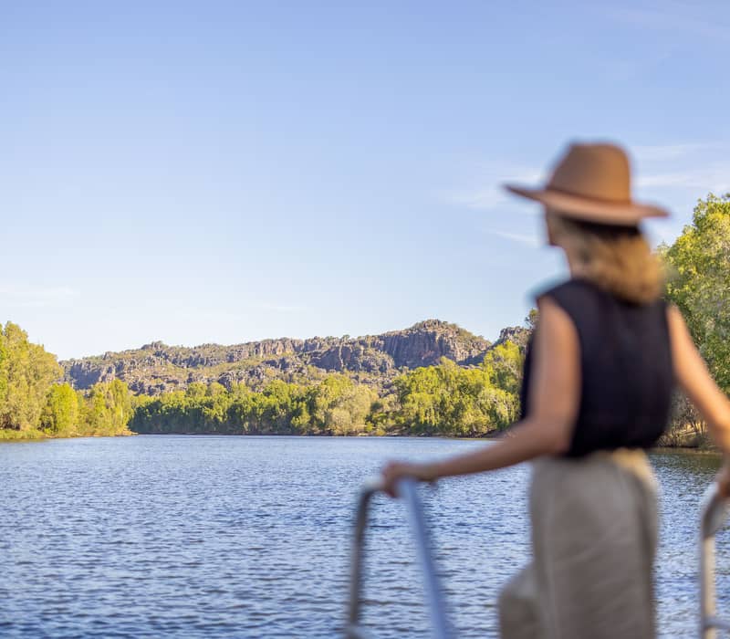 Silhouette of a woman in a hat looking out at the Kakadu landscape from a boat.