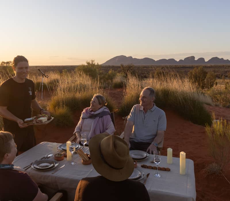 Luxury tent interior with a bed and open deck looking out over the Australian desert at sunset.