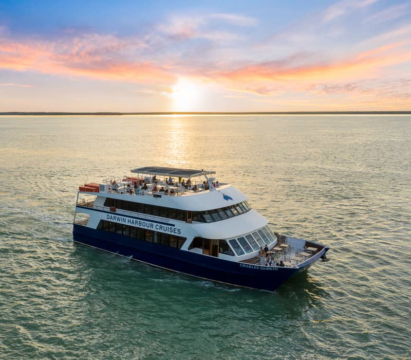 A luxury catamaran cruising Darwin Harbour during a vibrant tropical sunset in the Northern Territory.