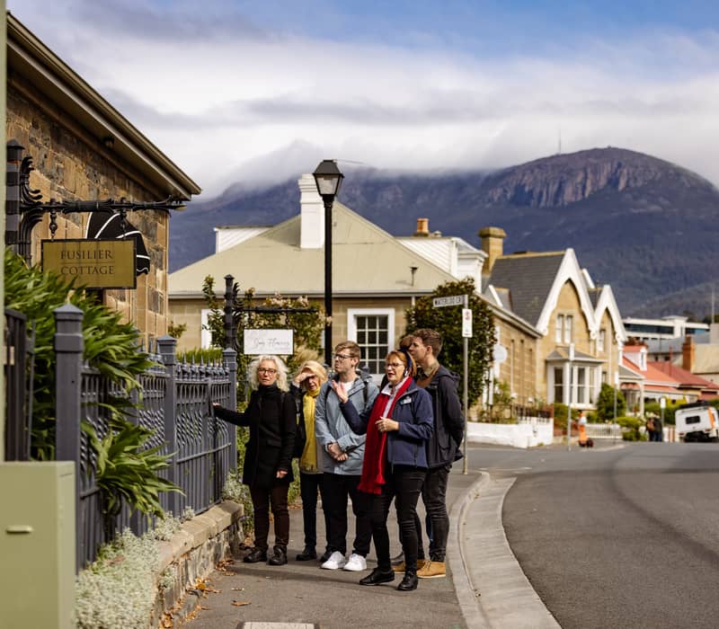 Guided tour group outside Fusilier Cottage in Battery Point with Mount Wellington visible in the distance.
