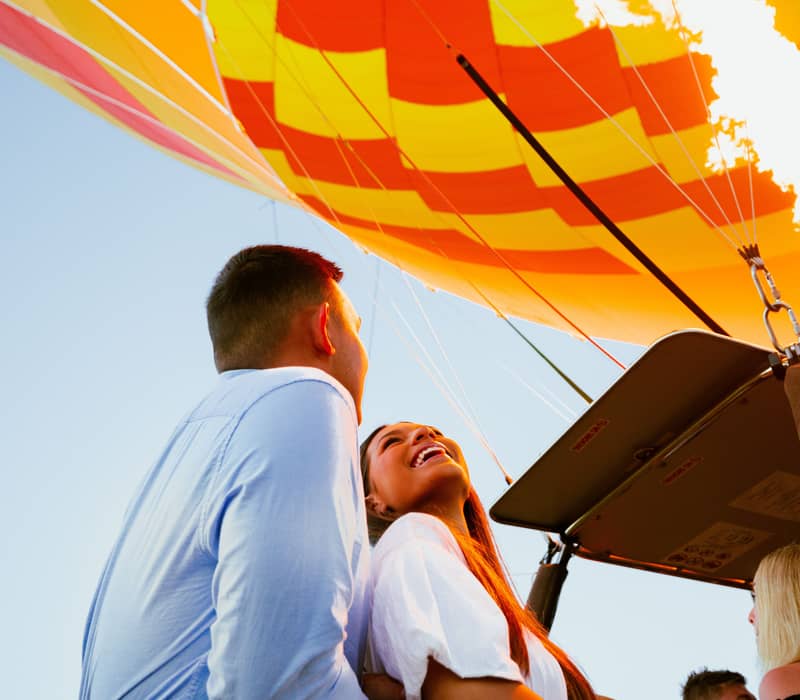 A smiling couple watches the hot air balloon burner ignite during a scenic morning flight over Canungra Valley.