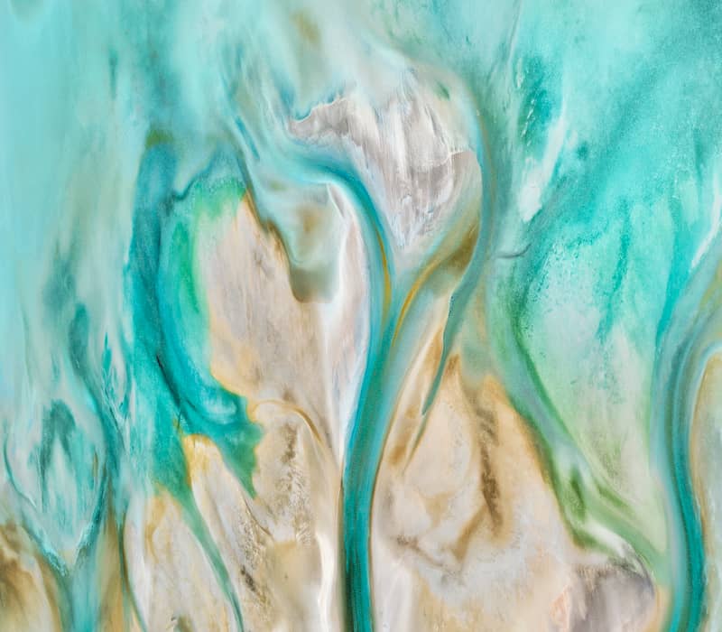 A top-down abstract aerial of white sand and bright turquoise water swirling together to create organic, flowing patterns.