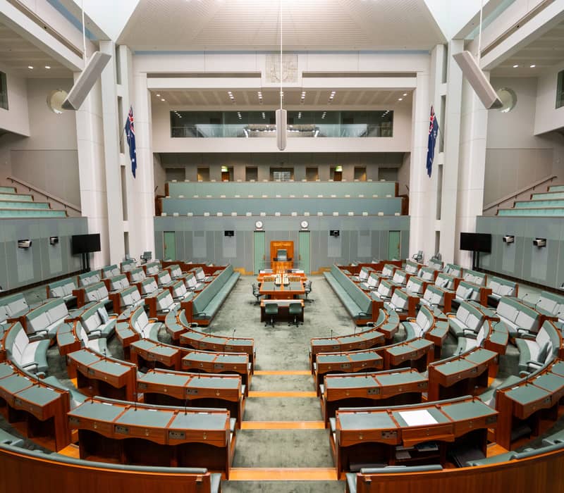 Interior view of the empty Australian House of Representatives chamber with its signature green seating and modern architectural lines.