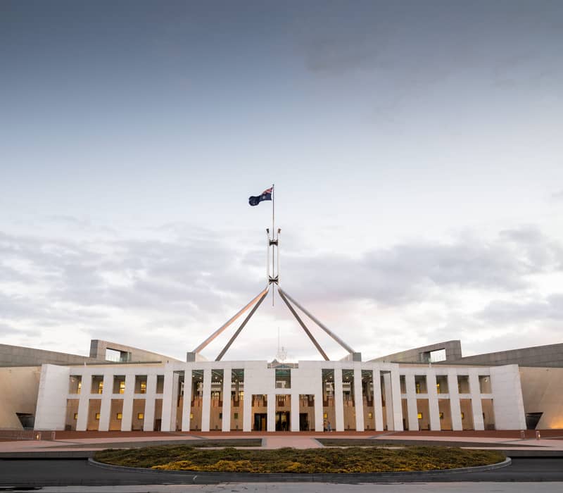 Sunset view of the Australian Parliament House on Capital Hill with lights illuminating the entrance and flagpole.