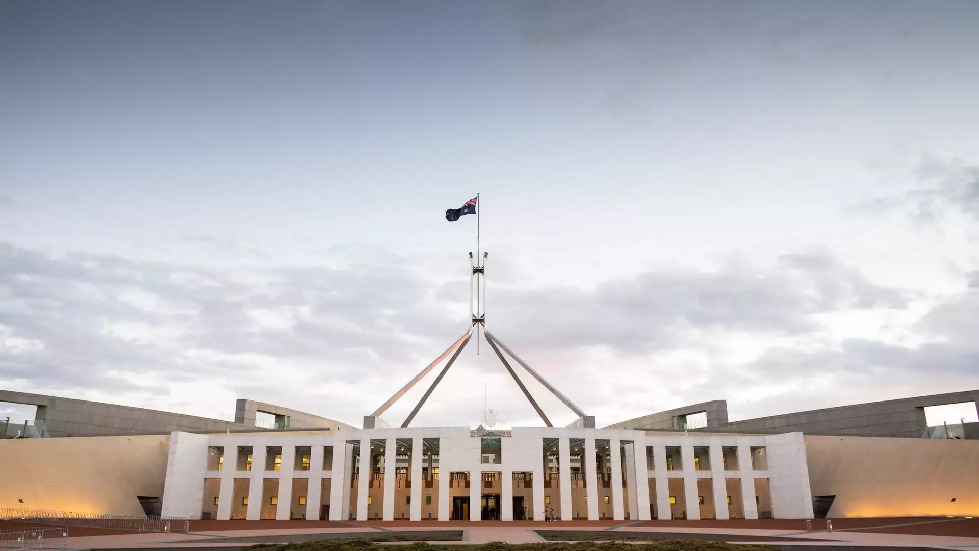 Sunset view of the Australian Parliament House on Capital Hill with lights illuminating the entrance and flagpole.