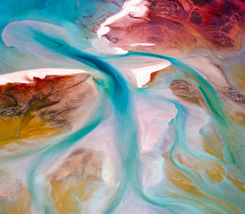 A vertical top-down aerial of swirling turquoise water channels cutting through white sandbanks and red earth.