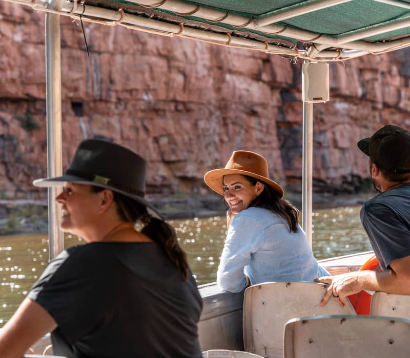 Tourists on a covered boat cruise through a narrow river gorge with high orange rock walls at El Questro.
