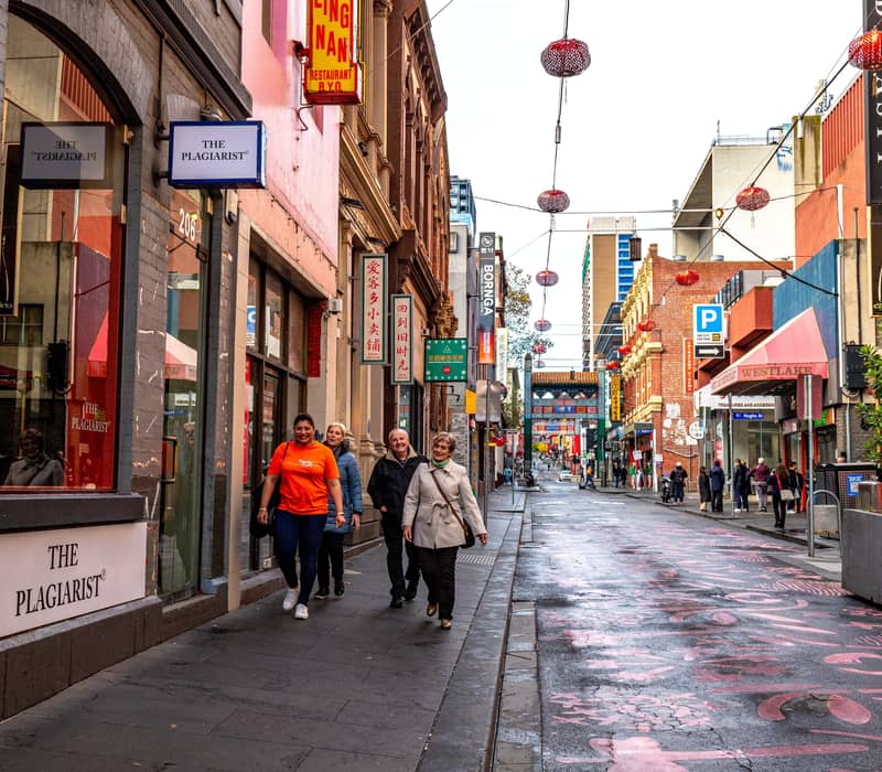 A small group of tourists walk down a Melbourne city lane adorned with red lanterns and Chinese signage during a guided food tour.