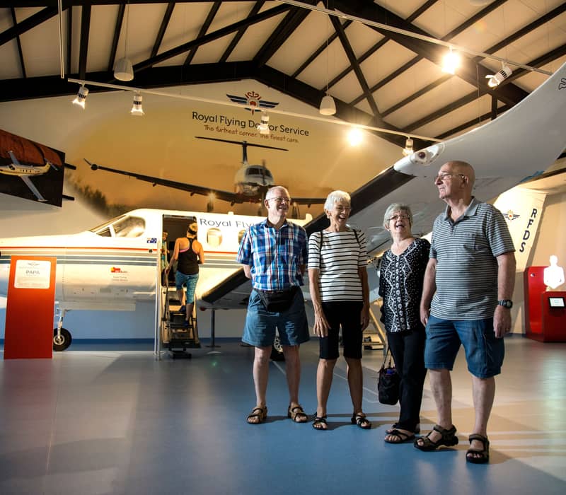 A group of senior travelers standing in front of a Royal Flying Doctor Service aircraft in a museum.
