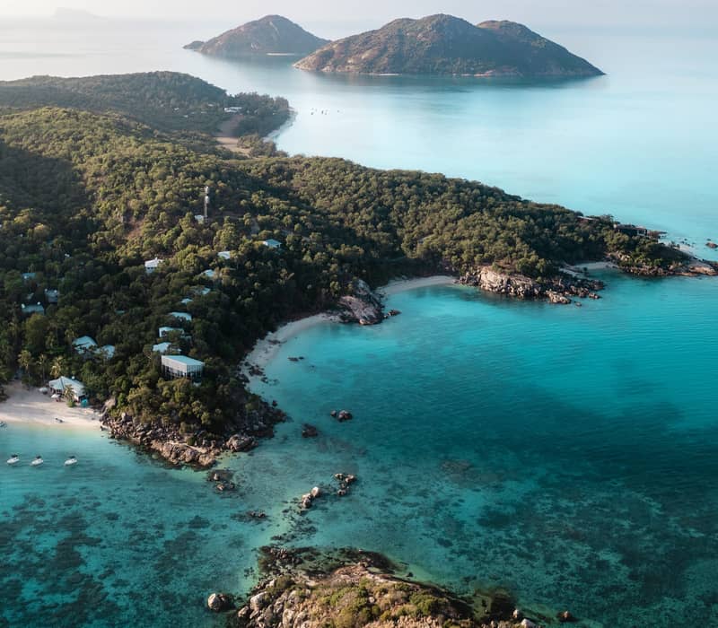 Spectacular aerial view of Lizard Island showing the resort, lush greenery, and vibrant blue reef water.