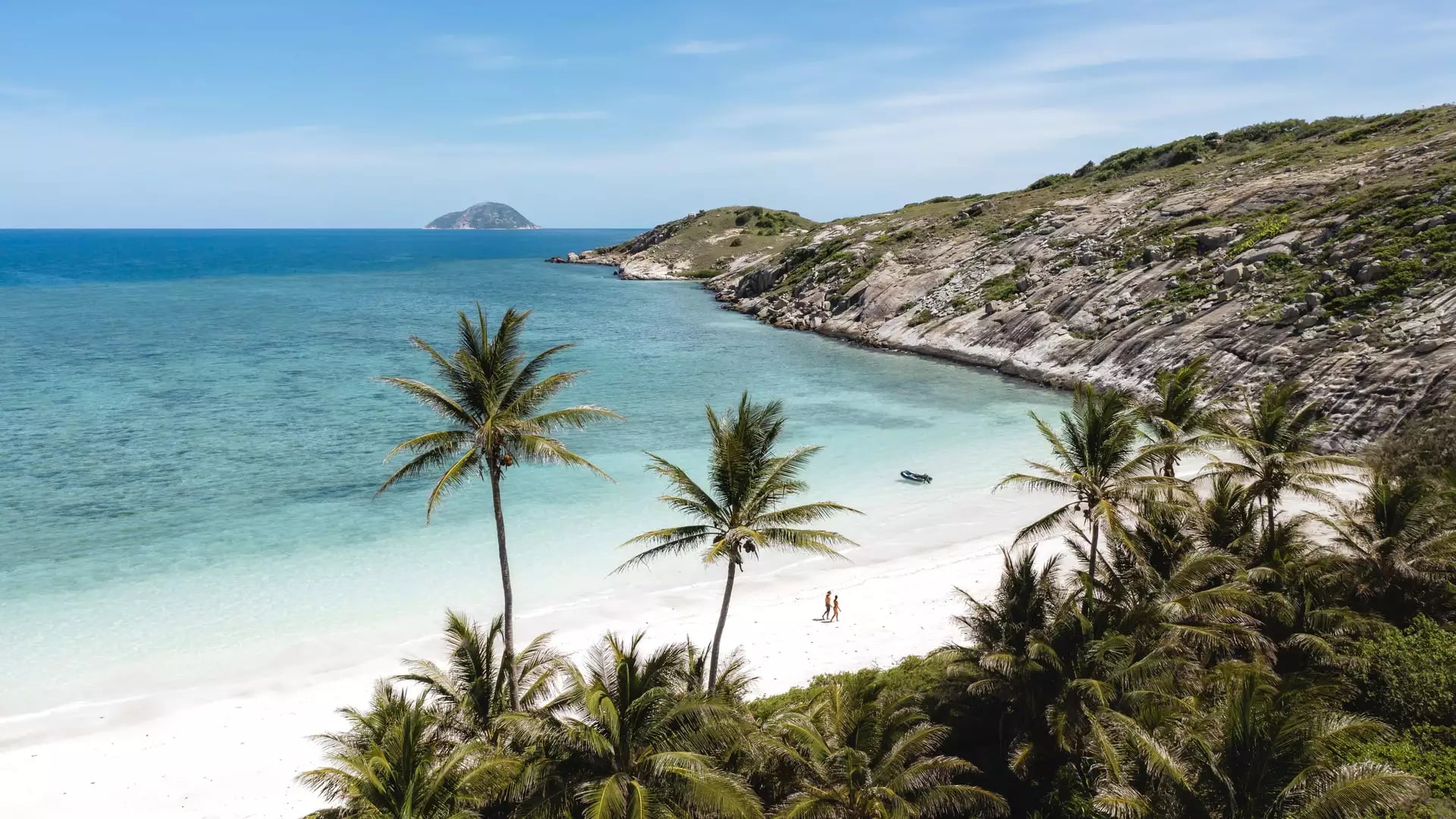 Aerial view of a white sand beach with palm trees and a couple walking by clear blue water on Lizard Island.