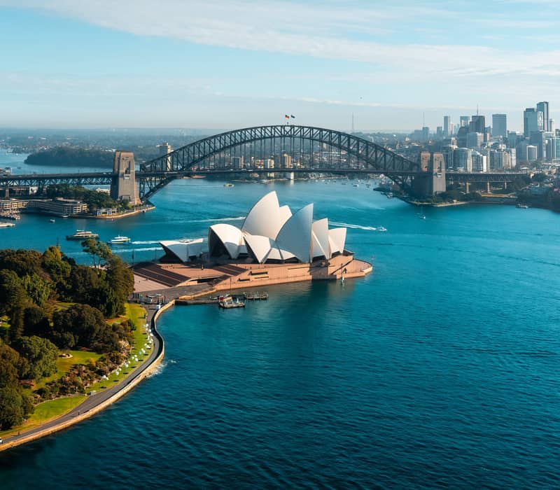 Aerial view of the Sydney Opera House and the Harbour Bridge with blue water and ferries in the harbor.