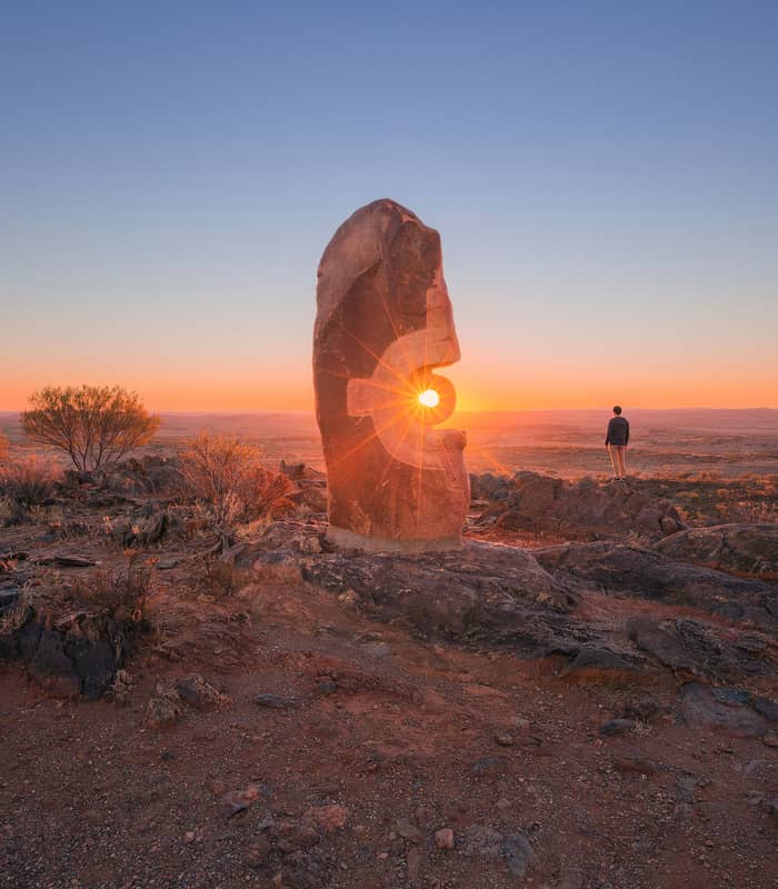 Carved sandstone sculptures standing on a hilltop overlooking the desert plains of Broken Hill under a clear sky.