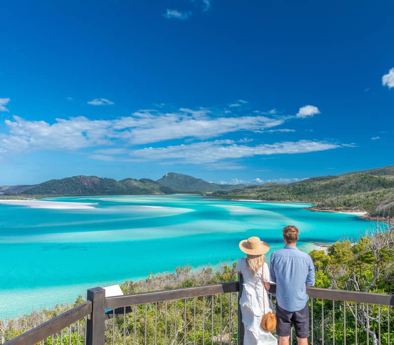 A man and woman looking out from a wooden balcony over the turquoise swirling sands of Hill Inlet.