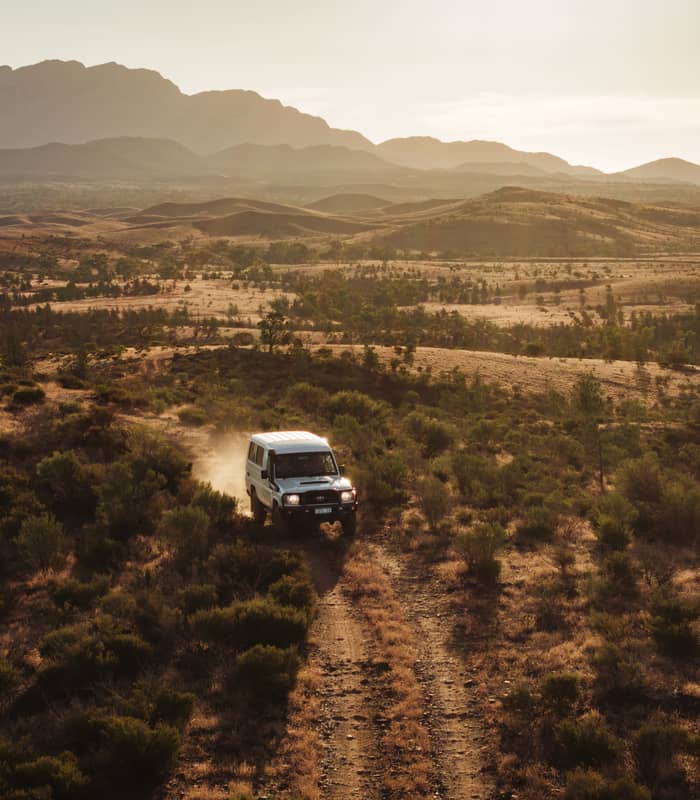 A 4WD vehicle driving through the golden-lit outback terrain of Rawnsley Park Station in South Australia.