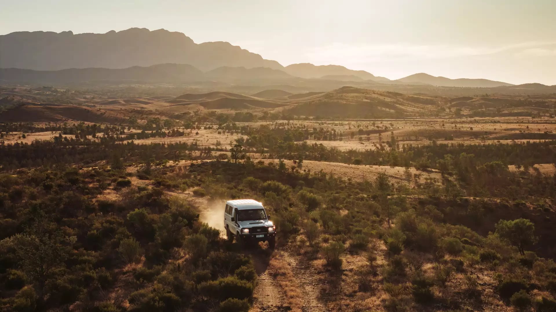 A 4WD vehicle driving through the golden-lit outback terrain of Rawnsley Park Station in South Australia.