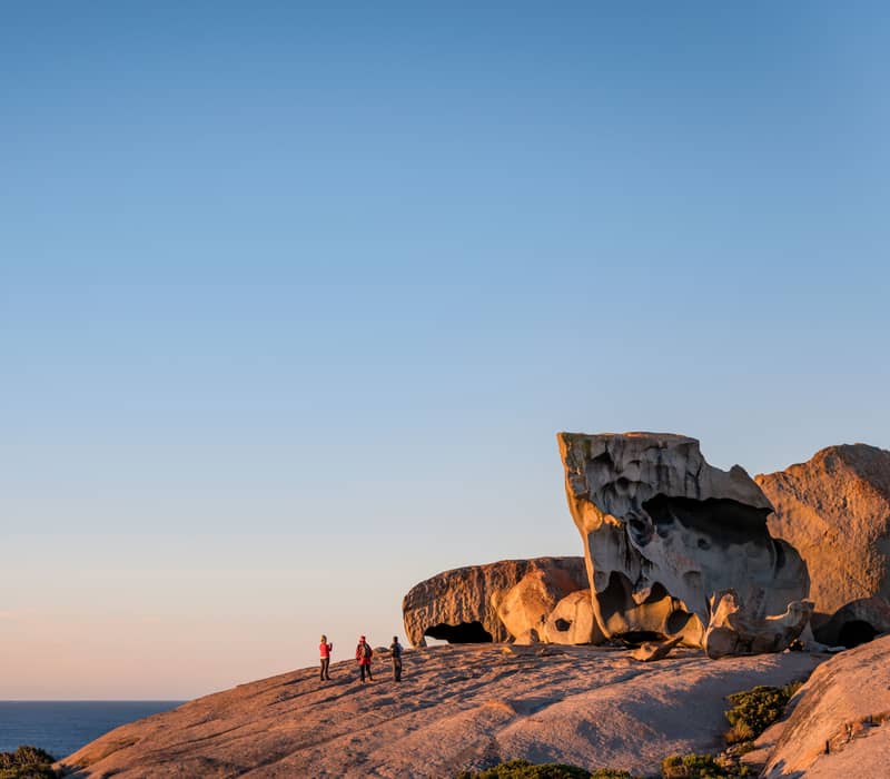 Travelers explore the iconic Remarkable Rocks granite formations on Kangaroo Island at golden hour.