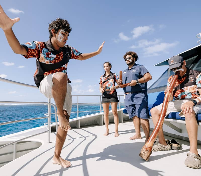 Indigenous rangers perform traditional dances and play the didgeridoo on a boat deck at the Great Barrier Reef.