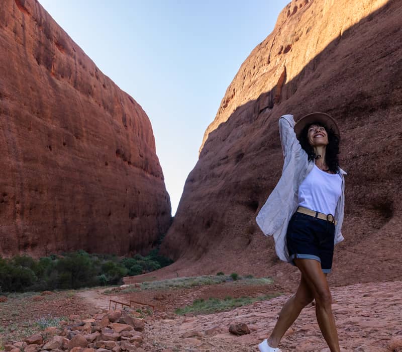 A woman in a hat walking through the massive, steep red walls of Walpa Gorge in the Northern Territory.