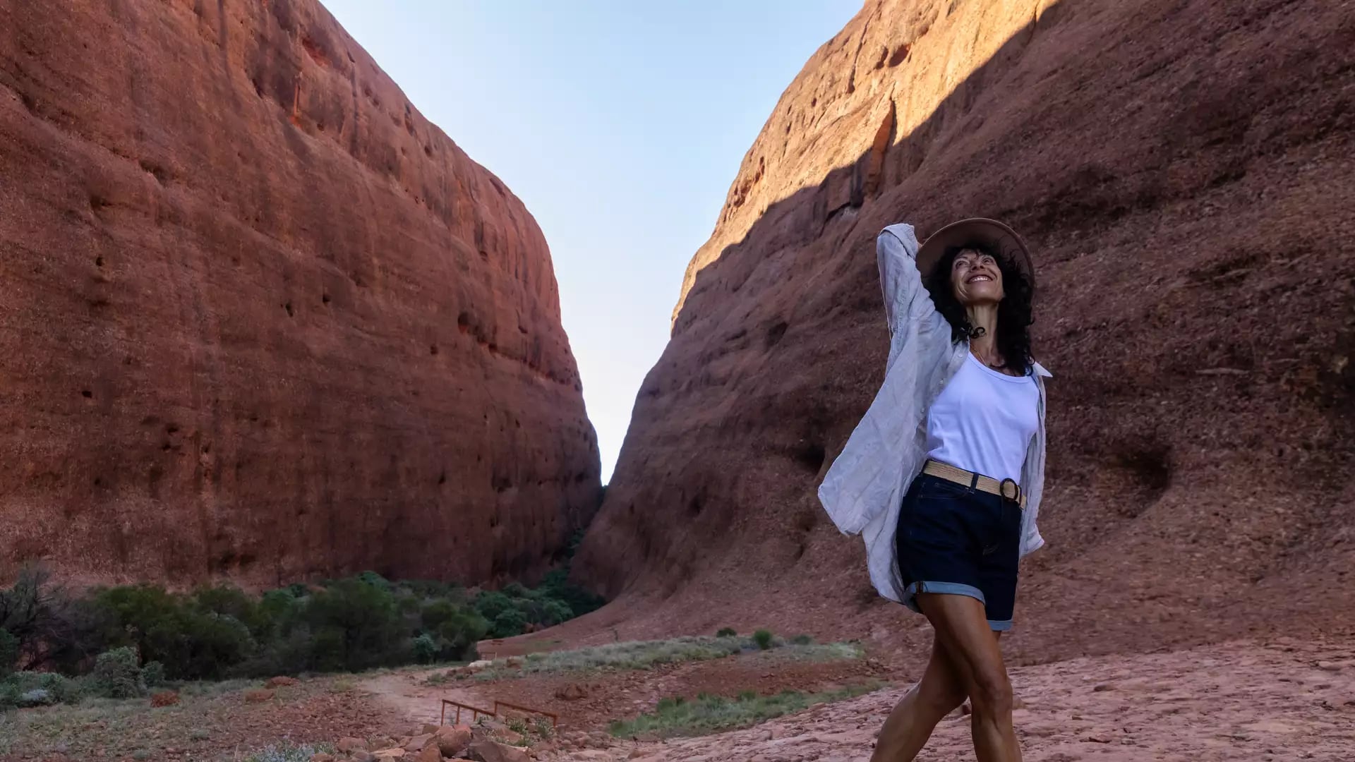 A woman in a hat walking through the massive, steep red walls of Walpa Gorge in the Northern Territory.