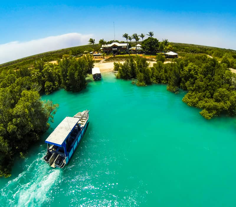 An aerial view of a tour boat navigating the bright blue tidal waters of Willie Creek Pearl Farm surrounded by green mangroves in the Kimberley.