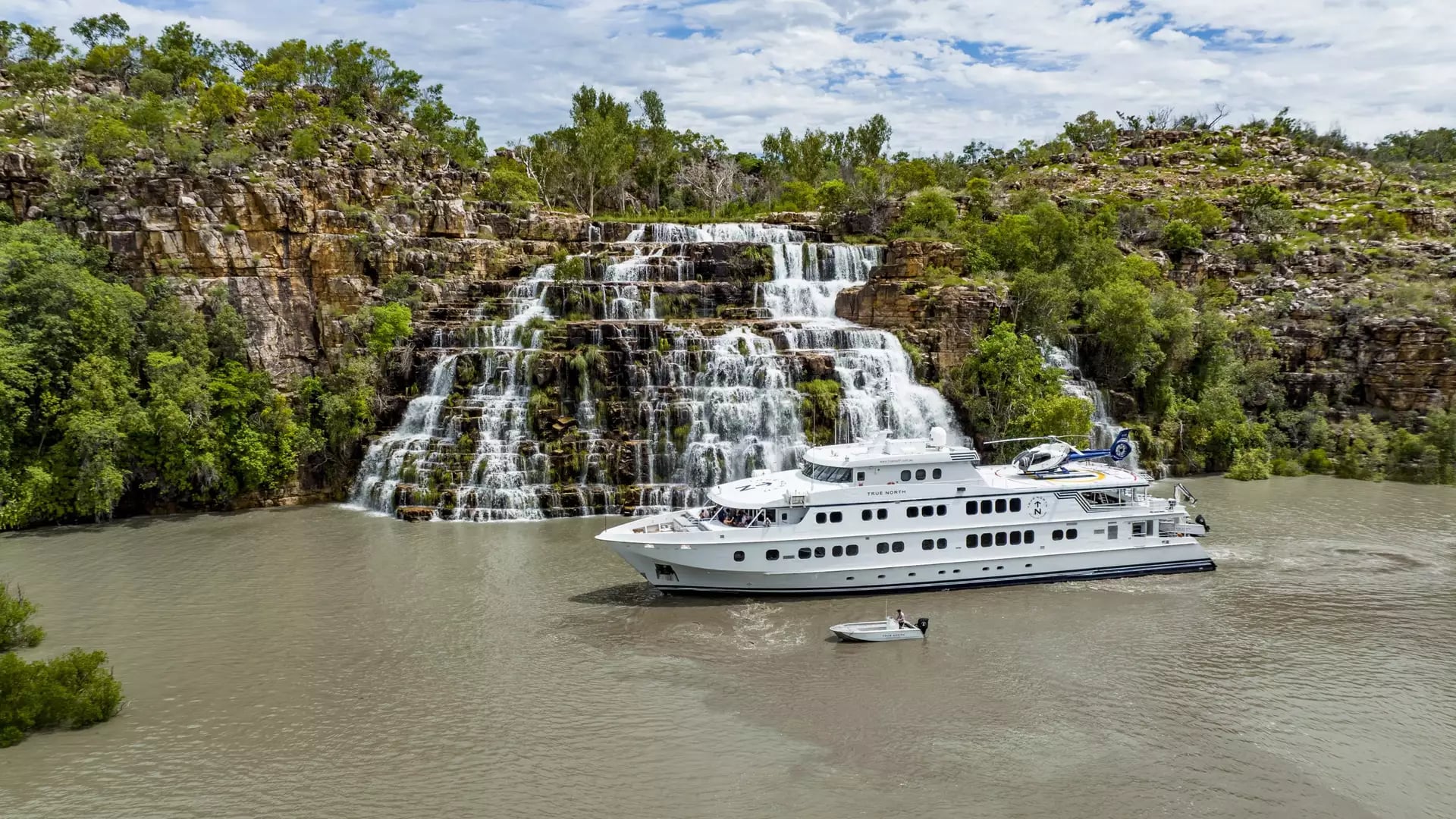 A luxury True North cruise ship positioned in front of a massive tiered sandstone waterfall in the Kimberley.