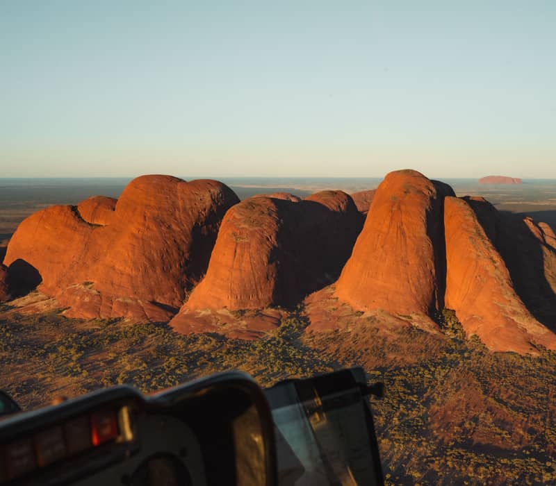 A stunning aerial perspective of the ancient conglomerate rock domes of Kata Tjuta, captured at golden hour from a helicopter cockpit.