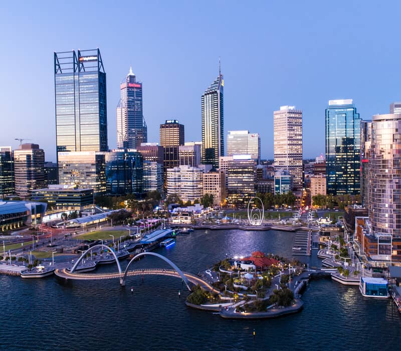 A twilight view of the glowing Perth city lights and Elizabeth Quay bridge reflected in the water.