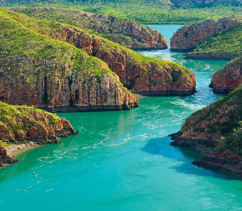 Panoramic landscape of turquoise water rushing through narrow red rock mountain gaps at Horizontal Falls, Western Australia.
