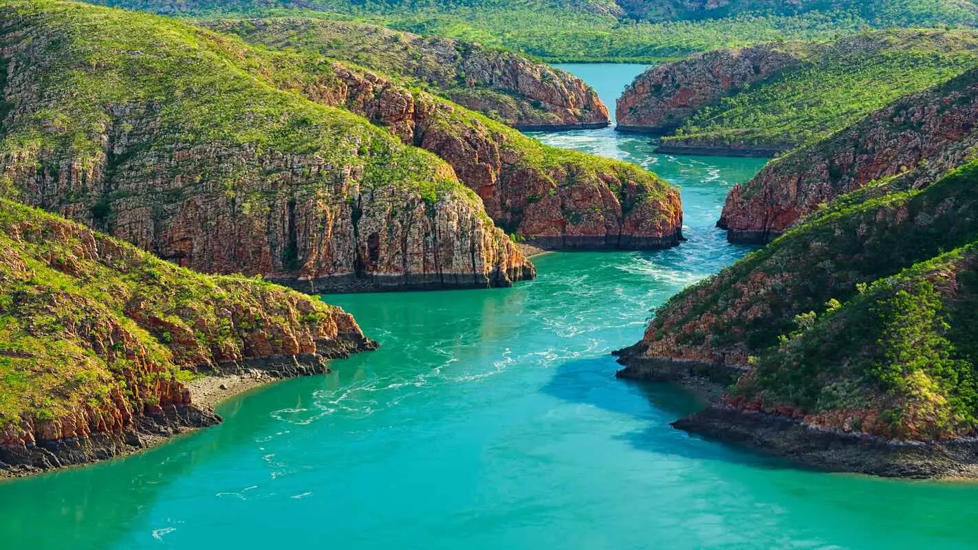 Panoramic landscape of turquoise water rushing through narrow red rock mountain gaps at Horizontal Falls, Western Australia.