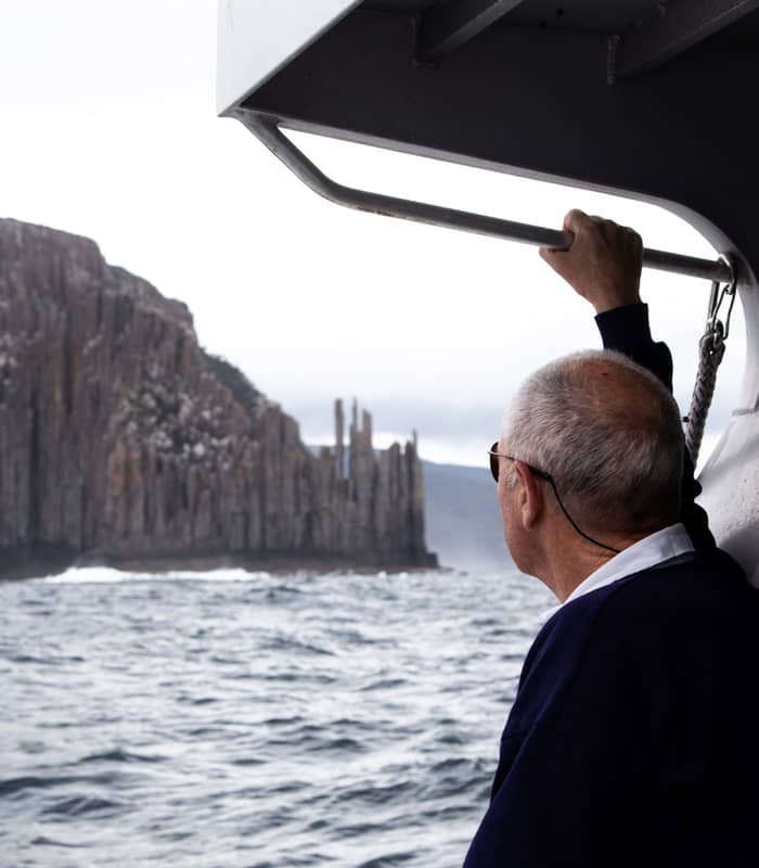 A passenger on an On Board Expedition Cruise gazes at the towering sea cliffs of Cape Raoul on the coast of Tasmania.