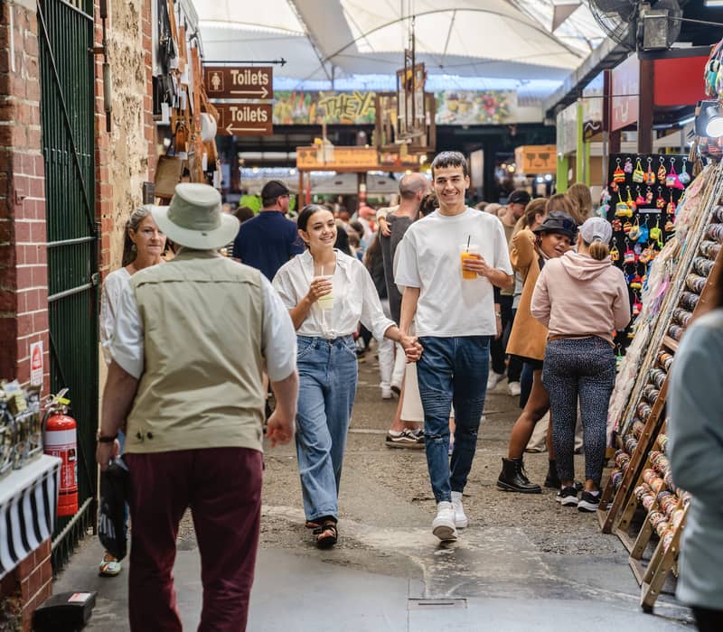 A man and woman walking through a busy indoor market aisle with stalls and shoppers in Fremantle.