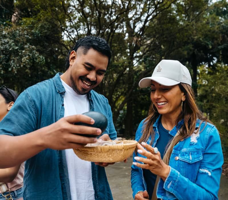 A man and woman smiling while examining a large dark emu egg during a cultural tour in Sydney.