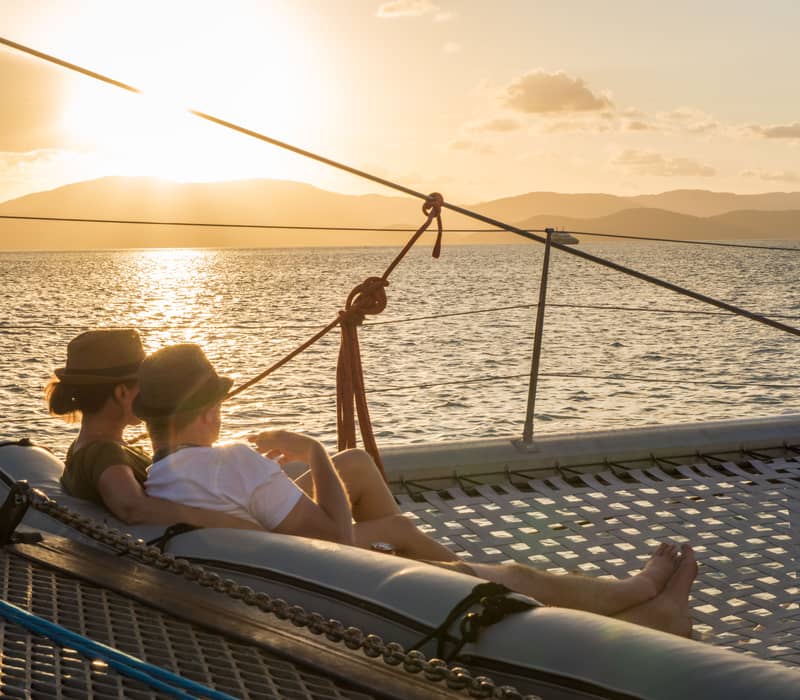 Couple sitting on a boat deck at sunset overlooking the calm waters of the Whitsunday Islands.