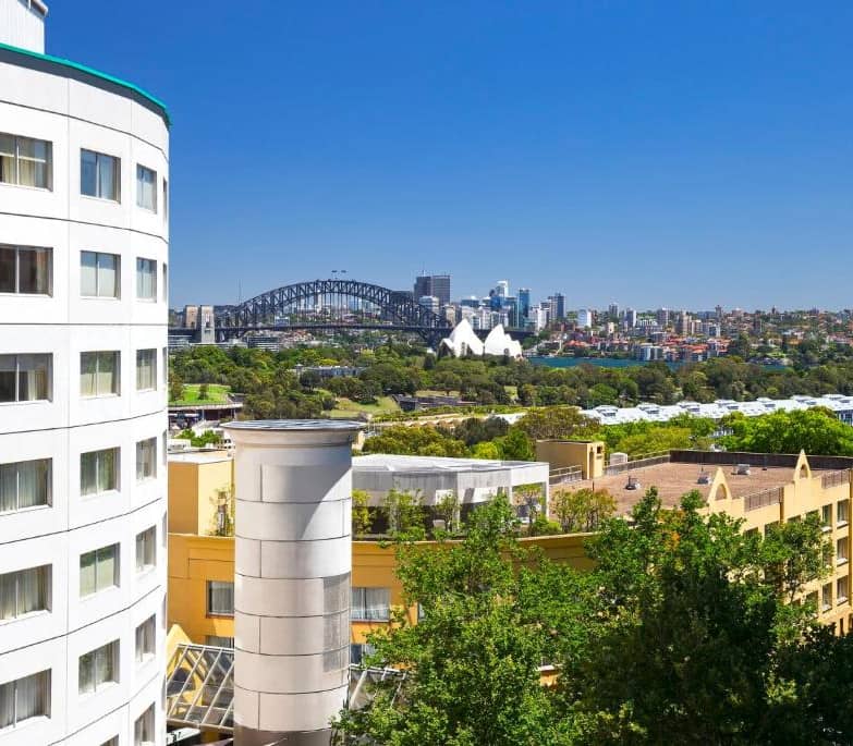 Premium hotel room with a king bed and a large window overlooking the Sydney Harbour Bridge and skyline.